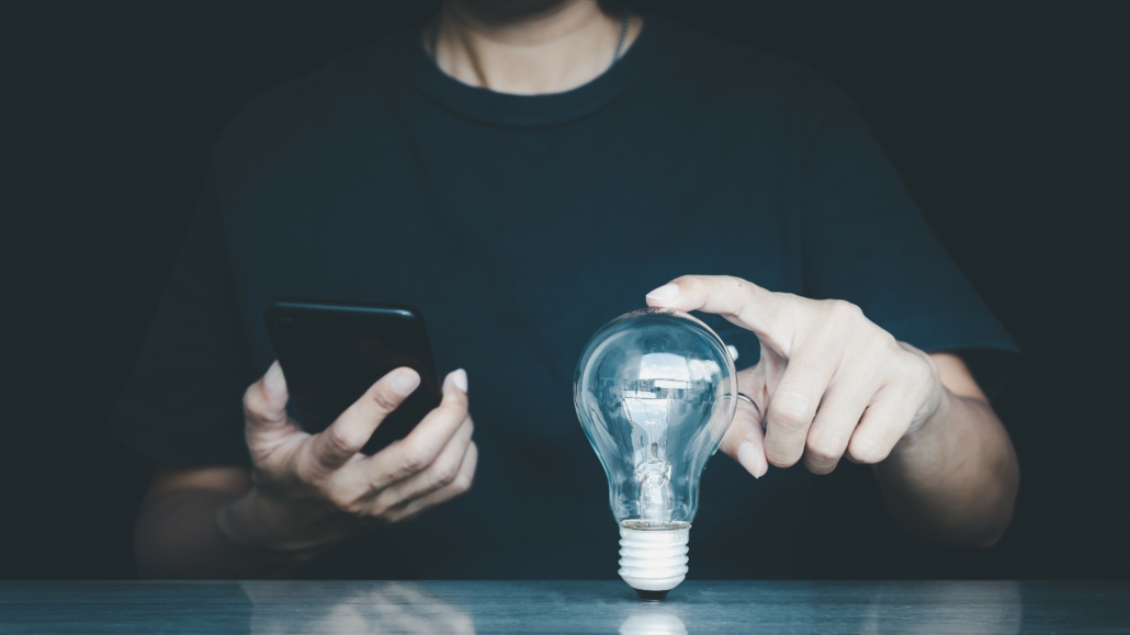 Ein Mann hält sein Smartphone in der einen und eine Glühbirne in der anderen Hand